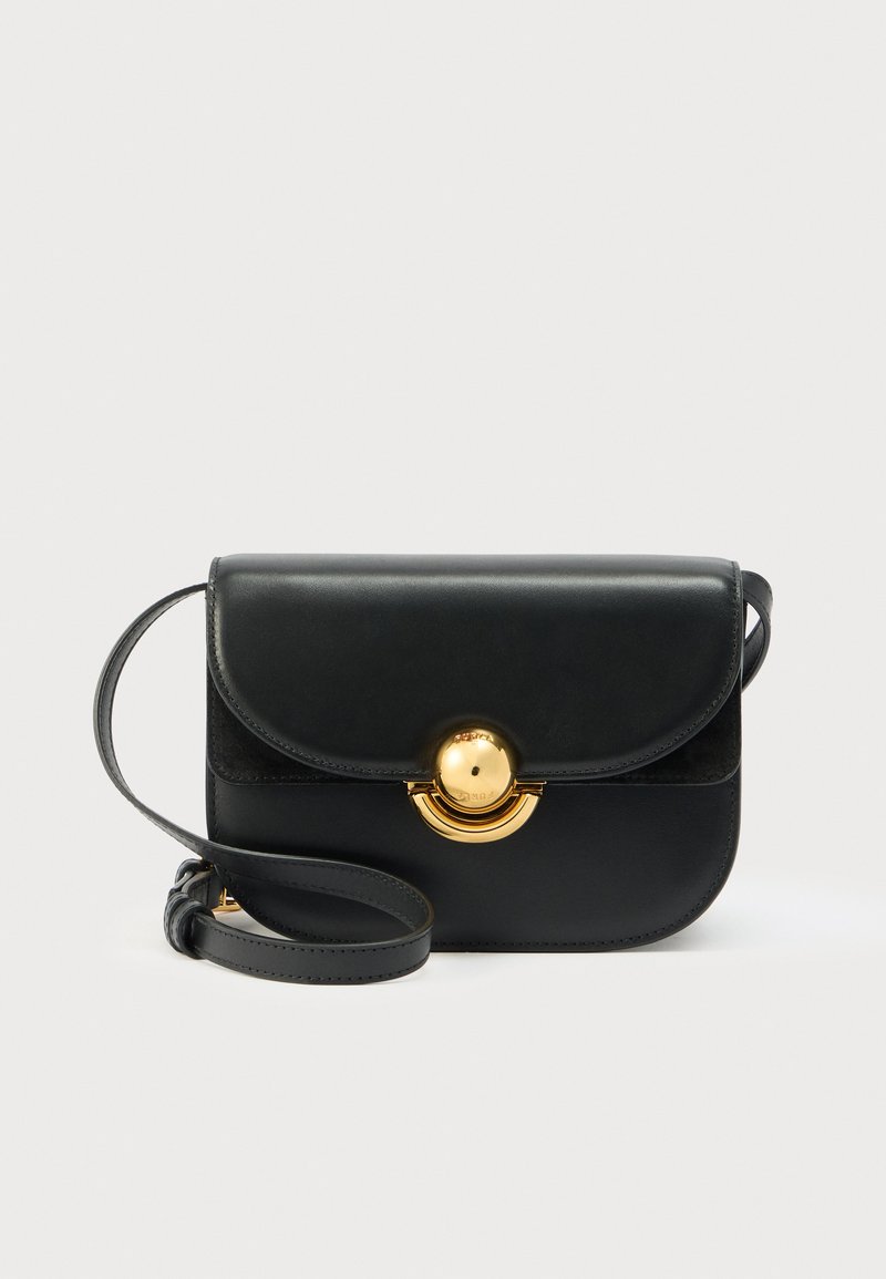 Schwarze Leder-Umhängetasche mit gewellter Klappe und rundem goldfarbenem Verschluss, mit verstellbarem Riemen, vor weißem Hintergrund.