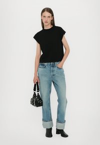 Black short-sleeve, boxy t-shirt paired with light blue, rolled-up denim jeans. Accessorized with a small black handbag and ankle boots.
