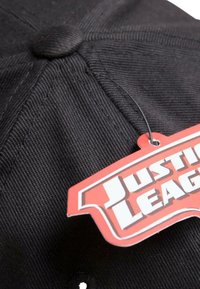 Crna bejzbol kapa s teksturiranim materijalom, koja ima okrugli gornji dugmadi i crveno-bijelu oznaku "Justice League" pričvršćenu.