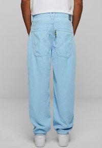 Light blue corduroy pants with a relaxed fit, featuring two back pockets and a colorful striped detail on the right pocket's edge.