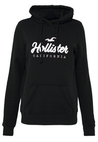 Svart hoodie med framficka, dragsko på huvan och vit text "Hollister" med rosa accent. Mjuk tyg med ribbade muddar.