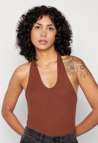 Camisola castanha com nervuras, de decote em V profundo e alças largas, combinada com calças pretas de cintura alta e texturizadas. Colar simples de corrente visível.