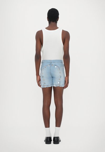 Shorts en denim de couleur bleu clair avec un ourlet effiloché, dotés de boutons argentés décoratifs sur les côtés. Associés à un débardeur blanc et des chaussettes.