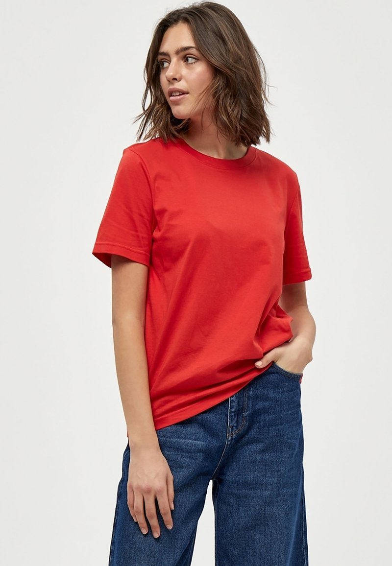 T-shirt in cotone rosso con maniche corte, scollo rotondo e vestibilità rilassata. Abbinato a jeans in denim blu per un look casual.
