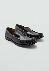 Mocasines de cuero negro con punta redondeada, flecos decorativos y acabado liso. Presentan un tacón bajo y resistente, con detalles de costuras mínimas.