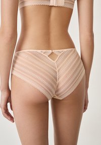 Koronkowy bikini w odcieniu nude, z poziomymi paskami i małym centralnym wycięciem z tyłu. Gładka tekstura i delikatne wykończenia.