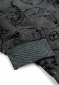 Tessuto in peluche grigio scuro con contorni di animali neri. Il polsino mostra una texture a costine grigio scuro, che garantisce una vestibilità aderente.