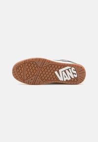 Fekete gumi cipőtalp gyémántmintázattal, fehér "VANS" logóval és barna gumi külső talppal. Simább textúra, nincs további részlet.