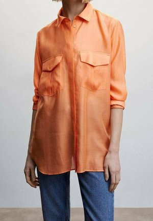 Oranges Hemd mit Knöpfen, zwei Brusttaschen, aufrollbaren Ärmeln und einer glatten Textur. Getragen mit blauen Denimjeans.