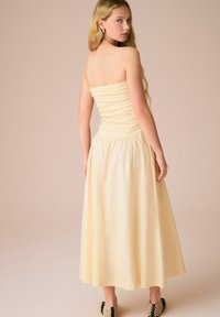 Strapless, geplooide gele jurk met een uitlopende, enkel-lange rok. Soepele textuur, aansluitende bovenkant en elastische tailleband voor comfort.