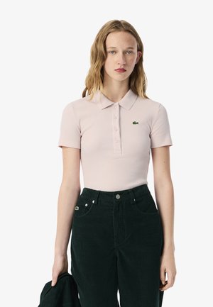 Polo shirt rosa pallido a coste con maniche corte e pattina dei bottoni, con un piccolo logo verde di Lacoste. Abbinato a pantaloni in corduroy verde scuro.