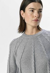 Grauer Ripp-Strickpullover mit ribbed Rundhalsausschnitt, der erhabene strukturierte Muster entlang des Körpers für zusätzlichen Detailreichtum aufweist.