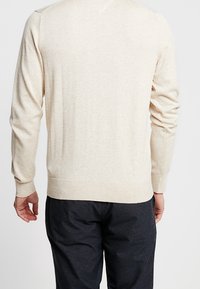 Beżowy sweter z długimi rękawami, ściągaczami na mankietach i u dołu, wykonany z miękkiego dzianinowego materiału. Tył ma prosty wzór bez ozdób.