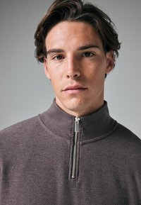Pull-over mi-zip violet clair avec une finition texturée et un col montant. Il présente une fermeture éclair en argent et un design simple et épuré.