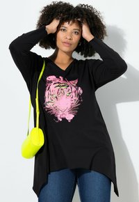 Chemise noire à manches longues et décolleté en V avec un graphique de tigre rose aux yeux verts. Associée à un petit sac bandoulière néon jaune.