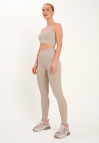 Beiges, geripptes Sport-Bra und Leggings-Set mit verstellbaren Trägern, hohem Bund und dezentem Logo. Kombiniert mit grauen Turnschuhen.