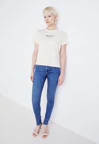 Stripet gul og hvit t-skjorte med korte ermer og rund hals, med "Pepe Jeans" trykket i svart. Kombinert med blå smale jeans.