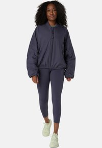 Marineblau bomberjacke mit Reißverschluss auf der Vorderseite, elastischem Saum und Seitentaschen, kombiniert mit passenden Leggings und hellen Sneakers. Glatte, elegante Textur.