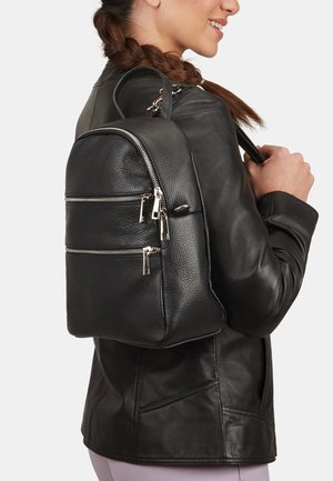 Mochila de cuero negro con dos bolsillos frontales con cremallera, de forma redonda y textura suave, llevada sobre una chaqueta de cuero.