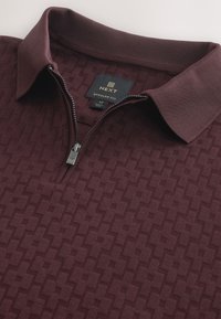 Polo bordeaux con zip, motivo a trama, collo e polsini a costine, con cerniera argento dotata di cursore brandizzato, vestibilità regolare.