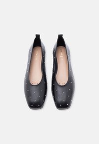 Μαύρα δερμάτινα παπούτσια μπαλαρίνες με ασημένιες καρφίτσες, στρογγυλεμένες τετράγωνες μύτες και μπεζ εσωτερικά πέλματα με τη φίρμα "Geox Respira", απεικονιζόμενα από πάνω σε λευκό φόντο.