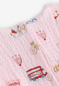 Tela de color rosa claro con textura y pequeños cierres de botones, con estampados de coronas, un autobús de dos pisos rojo y animales que llevan bufandas.