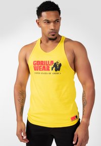 Rumena majica brez rokavov z črnim grafičnim motivom gorile in rdečim napisom "GORILLA WEAR" ter "ZDA"; mehak material in prilegajoč kroj.