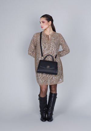 Borsa a tracolla in pelle nera con hardware dorato. Il modello indossa un vestito beige con dettagli in paillettes argentate e stivali neri fino al ginocchio.