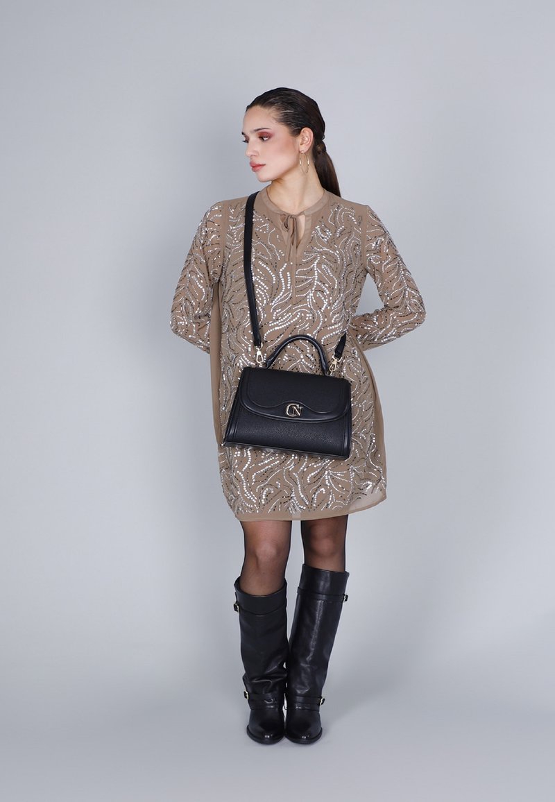 Borsa a tracolla in pelle nera con hardware dorato. Il modello indossa un vestito beige con dettagli in paillettes argentate e stivali neri fino al ginocchio.