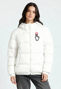 Giacca a vento bianca imbottita con chiusura frontale a zip, cappuccio e imbottitura in piuma d'oca. Presenta una grafica a mano "cuore" nera e rossa sul petto.