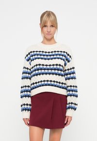 Strickpullover in Creme mit blauen und schwarzen horizontalen Streifen, ausgestattet mit Rundhalsausschnitt und gerippten Bündchen, kombiniert mit einem bordeauxfarbenen plissierten Rock.