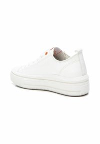 Zapatillas de lona blancas con una superficie texturizada, suela de goma y tacón grueso. Los detalles incluyen ojales naranjas y un lazo en la parte trasera para facilitar su uso.