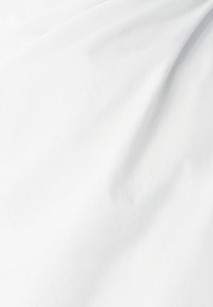 Bílá tkanina s hladkou texturou, vykazující jemné záhyby a subtilní variace ve světle, naznačující lehký a vzdušný materiál.