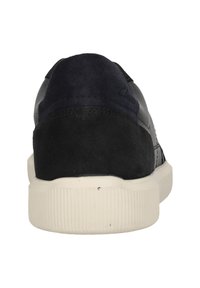 Bakifrån av en svart sneaker med en mockahäl och vit räfflad sula på en vit bakgrund.