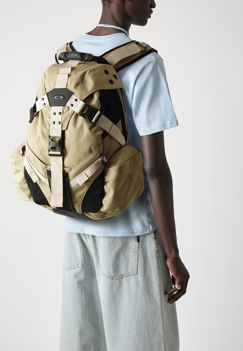 Khaki-Rucksack mit doppelt Mesh-Seitentaschen, verstellbaren Trägern und schwarzen Akzenten. Leichtes Material mit einem eleganten, abgerundeten Design.