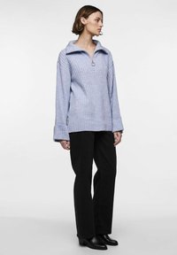 Svetlo modra rebrasta pulover s sprednjim zadrgo, širokimi rokavi in ovratnikom, v kombinaciji s črnimi širokimi hlačami in čevlji s peto.