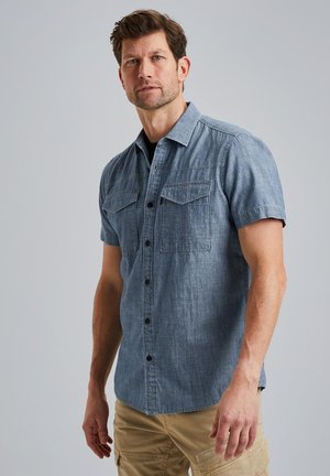 Camisa de manga corta, con botones, en denim azul claro, con dos bolsillos en el pecho, botones negros y un cuello clásico, con un corte informal.