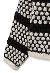 Schwarz-weißer gestrickter Pulloverwinkel mit einem strukturierten Muster aus erhabenen Punkten und abwechselnden Streifen, versehen mit einem naturfarbenen gerippten Bündchen.