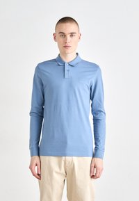 Dlhý rukáv polo tričko v svetlom modrom bavlnenom materiáli, s golierom, trojbuttonovou légou a malou nášivkou loga na hrudi.