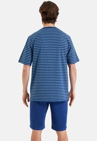 T-shirt rayé bleu à manches courtes, avec des rayures horizontales bleu ciel, associé à un short bleu uni. Tissu en coton doux.
