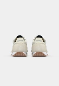 Svetlo béžové bežecké topánky s textúrovaným povrchom, bielou medzipodrážkou a hnedou gumovou podrážkou. Obsahuje logo "Reebok" na päte.