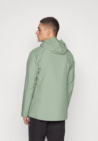Chaqueta verde claro con capucha, que presenta una textura suave y un diseño simple y aerodinámico. La parte trasera tiene un dobladillo ligeramente más largo.