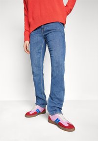 Modré džíny s rovný střih, zkombinované s barevnými retro teniskami s červenými, růžovými a modrými akcenty, obuté s červeným svetr.