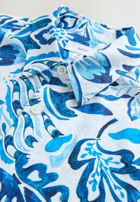 Kurzarmhemd mit einem blauen Blumenmuster auf weißem Hintergrund, aus einem strukturierten Stoff und mit zwei Knopfverschlüssen am Kragen.