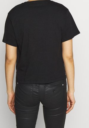 Person wearing a plain black short-sleeve shirt and black leather pants, shown from the back against a neutral background.