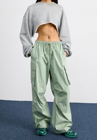 Grå cropped sweatshirt og løse lysegrønne cargo-bukser med lommer. Materialet ser blødt ud; bukserne har snor og elastisk talje.