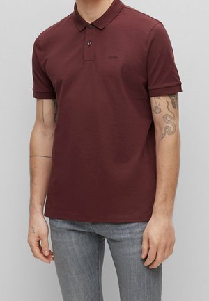 Bordová polo košile s klasickým límcem, dvouknoflíkovou légou a krátkými rukávy. Obsahuje malé tónové logo na hrudi. Hladká bavlněná tkanina.