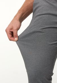 Pantalones de deporte grises con un tejido texturizado, mostrando la elasticidad mientras una mano tira de la pierna, resaltando la flexibilidad del material.