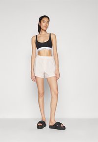 Černý bralet s logem Calvin Klein, světle růžové pruhované šortky, ploché černé sandály s širokými popruhy, hladká látka a volný střih.