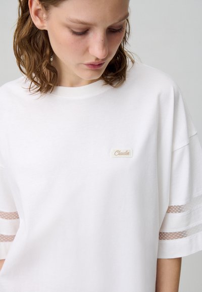 T-shirt bianca in cotone con vestibilità rilassata, caratterizzata da un piccolo etichetta ricamata e strisce in rete trasparente sulle maniche.